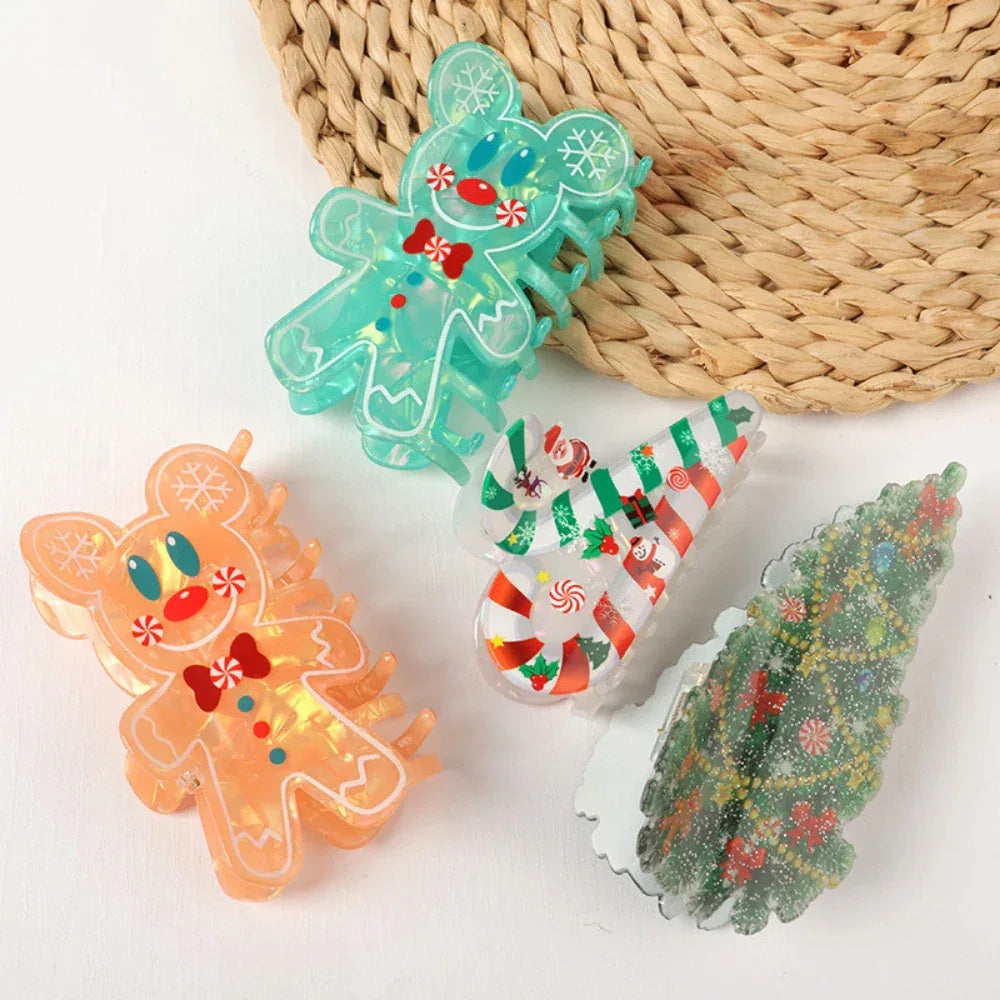 A collection of four Christmas-themed hair claw clips including two gingerbread men, a candy cane, and a Christmas tree, arranged on a woven placemat and a white surface.