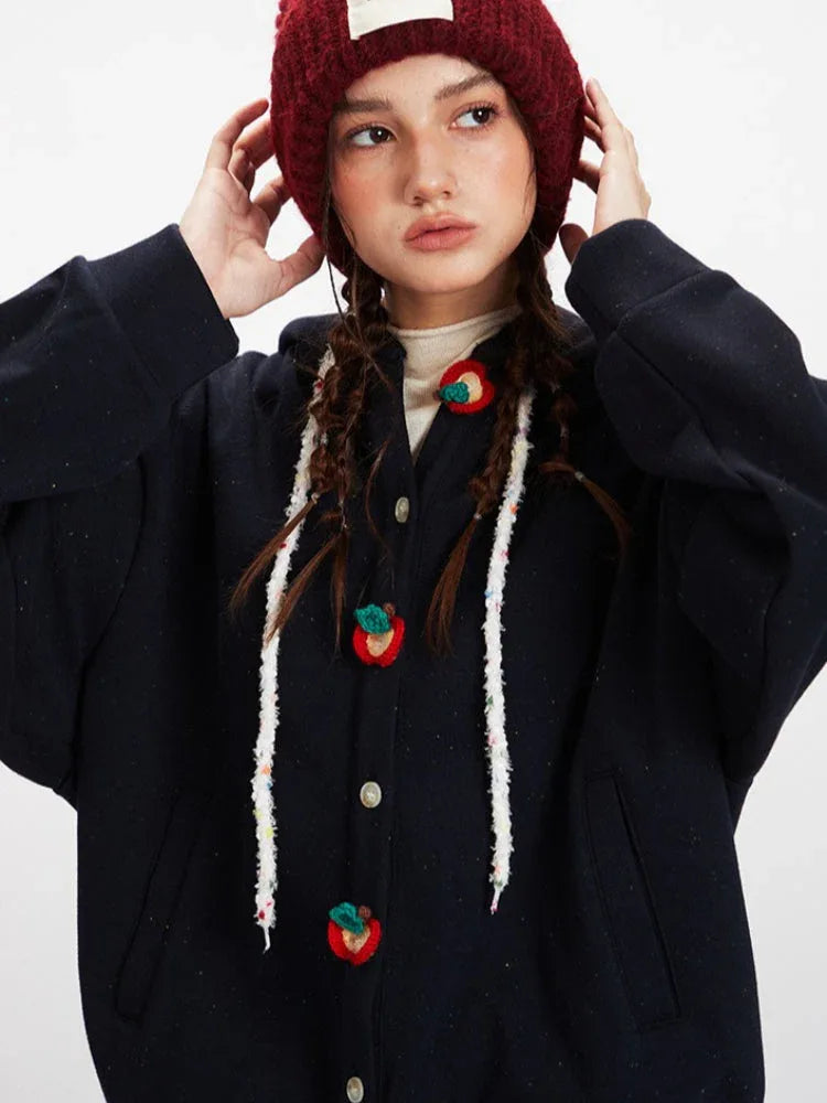 Close-up on the fruit-shaped buttons and drawstrings of a dark blue hooded cardigan.