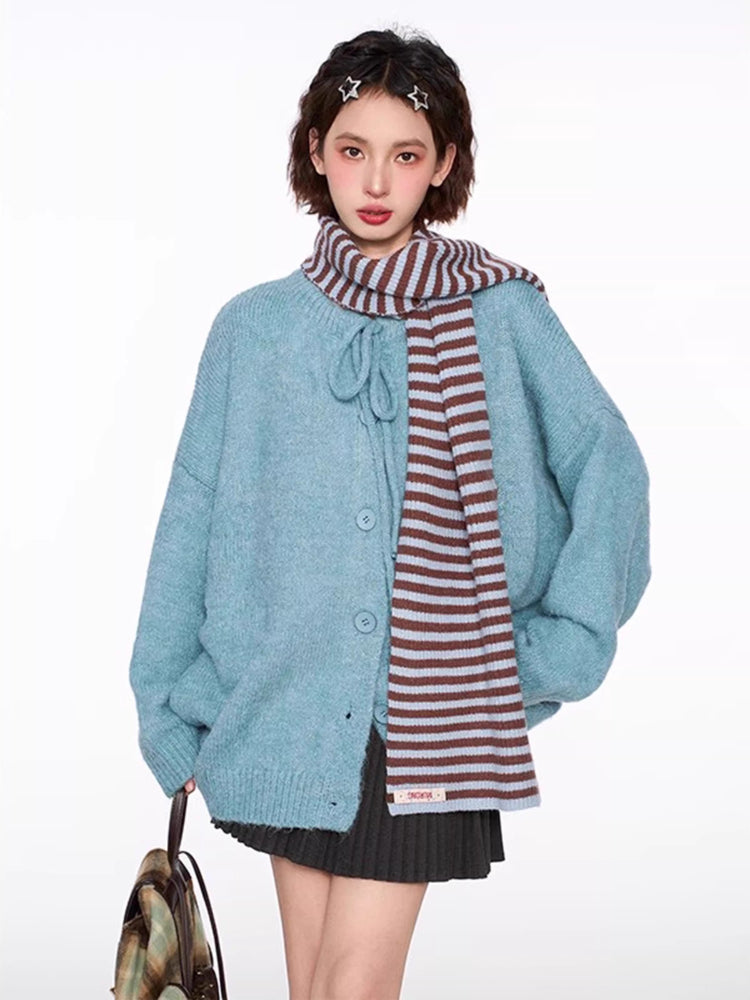 Woman wearing a light blue knit cardigan with tie neck and buttons, grey pleated skirt, brown crossbody bag, white leg warmers, and a striped scarf.