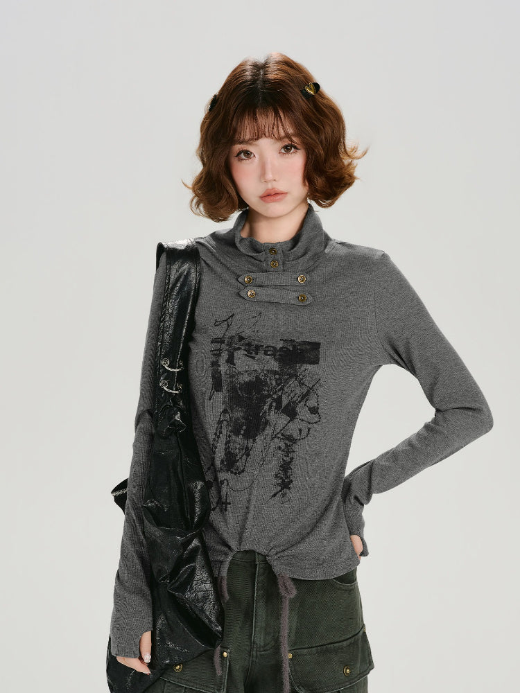 Woman wearing a grey long-sleeve graphic print turtleneck top with thumbhole cuffs and a drawstring hem, with a black bag slung over her shoulder.