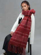 A woman is sitting while wearing a white sweater and a prominent red plaid scarf with fringe.