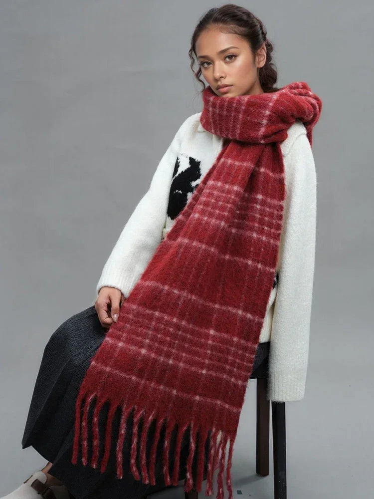 A woman is sitting while wearing a white sweater and a prominent red plaid scarf with fringe.