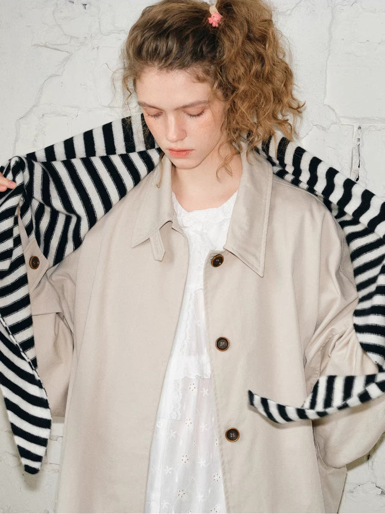 Model adjusting a black and white striped scarf over a beige coat