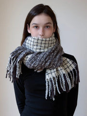 Close-up of a woman wearing a plaid scarf with fringe detail wrapped snugly around her neck.
