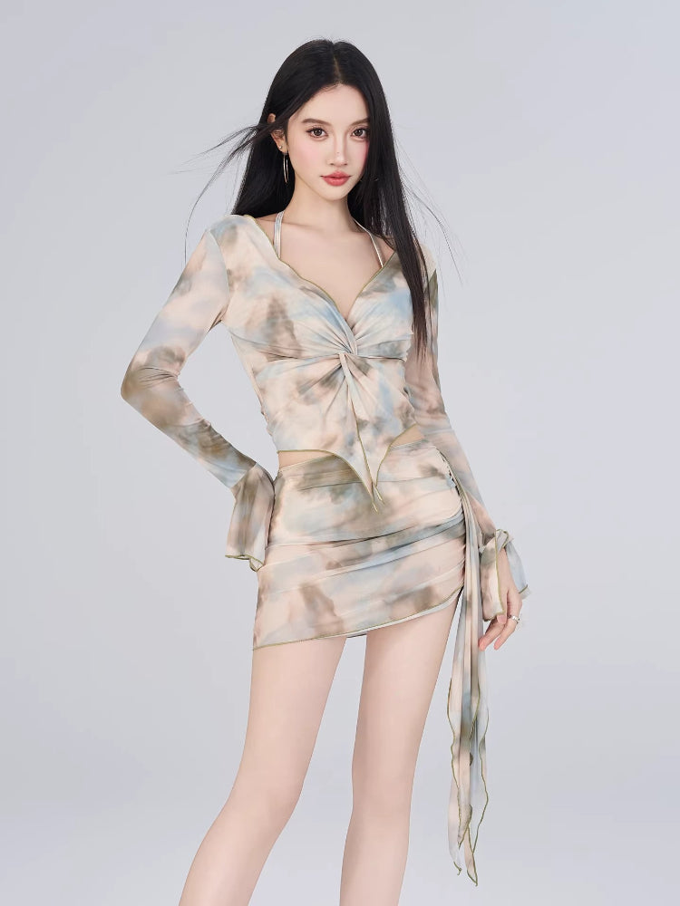 Full-body view of a woman in a sheer mesh abstract print two-piece set, highlighting the twisted front detail on the top and the ruched skirt.
