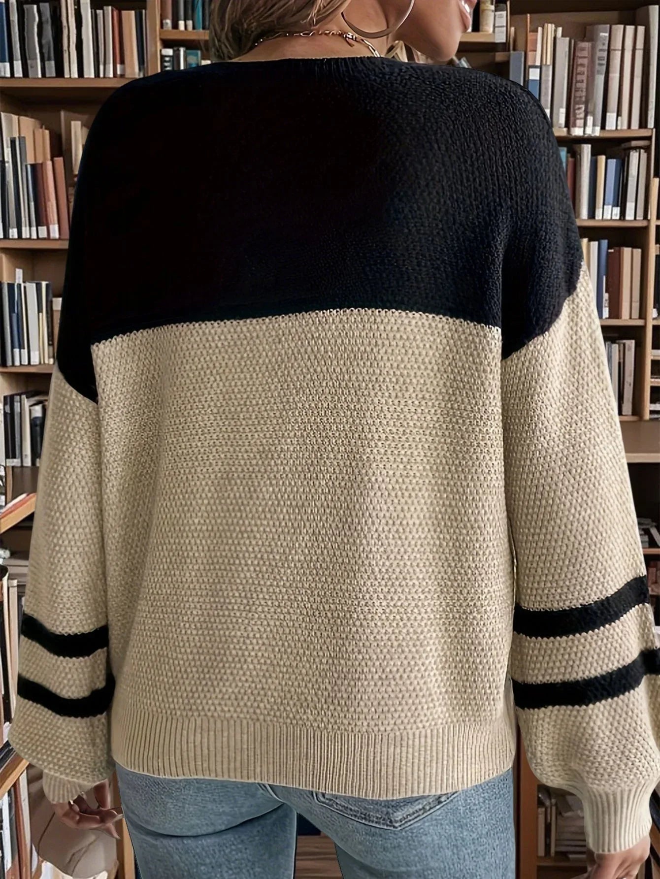Back view of a woman wearing a black and tan color-blocked sweater with striped sleeves, in front of a bookshelf.