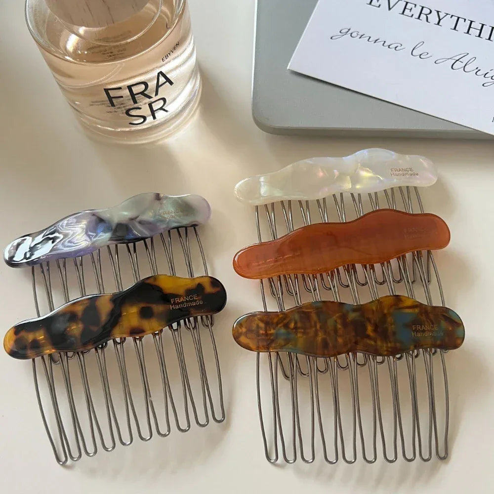A close-up view of several cloud-shaped hair combs in different colors, displayed on a white surface with a perfume bottle and a laptop.