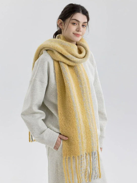 Woman wearing a yellow and gray striped scarf with fringe detail over a grey sweatshirt