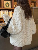 back view of a woman wearing an off-white chunky cable knit oversized sweater with a black handbag
