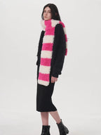 Side view of a model wearing a black sweater, black dress, and a pink and white striped fuzzy scarf.