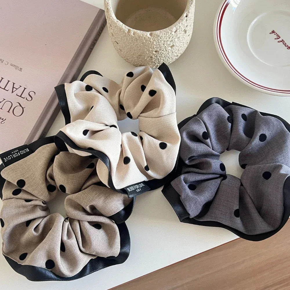 Two beige polka dot scrunchies and one gray polka dot scrunchie arranged on a white surface