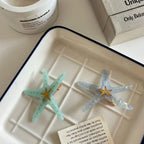 Two starfish hair clips, one light blue and one light grey, are displayed on a white tray.