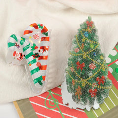 A candy cane hair clip and a Christmas tree hair clip shown on a white cloth with a striped Christmas-themed card.