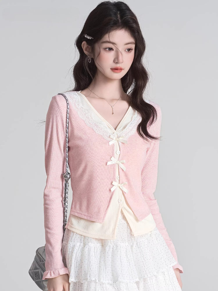 Woman wearing a pink V-neck knit cardigan with lace trim and bow closures over a cream-colored top and a white polka dot ruffled skirt.