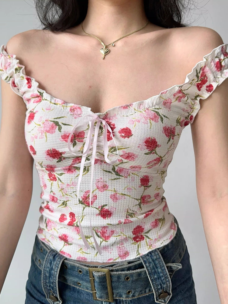 Close-up of a white floral print top with pink and red flowers, featuring ruffle trim and a tie front detail.