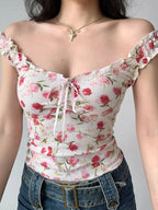 Close-up of a white floral print top with pink and red flowers, featuring ruffle trim and a tie front detail.