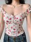 Close-up of a white floral print top with pink and red flowers, featuring ruffle trim and a tie front detail.