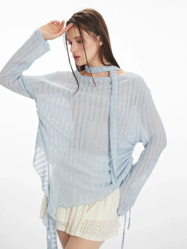 side view of a model wearing a light blue sheer knit sweater with an asymmetrical hem and a neck scarf, paired with a white lace skirt and white heels, holding a white handbag, posing with hand on forehead