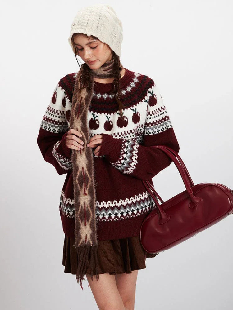 Close-up of a woman wearing a maroon and white knit sweater with an apple Fair Isle pattern, patterned scarf, and holding a maroon handbag.