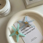 Two starfish hair clips, one light blue and one light grey, are arranged on a white tray with a piece of paper.