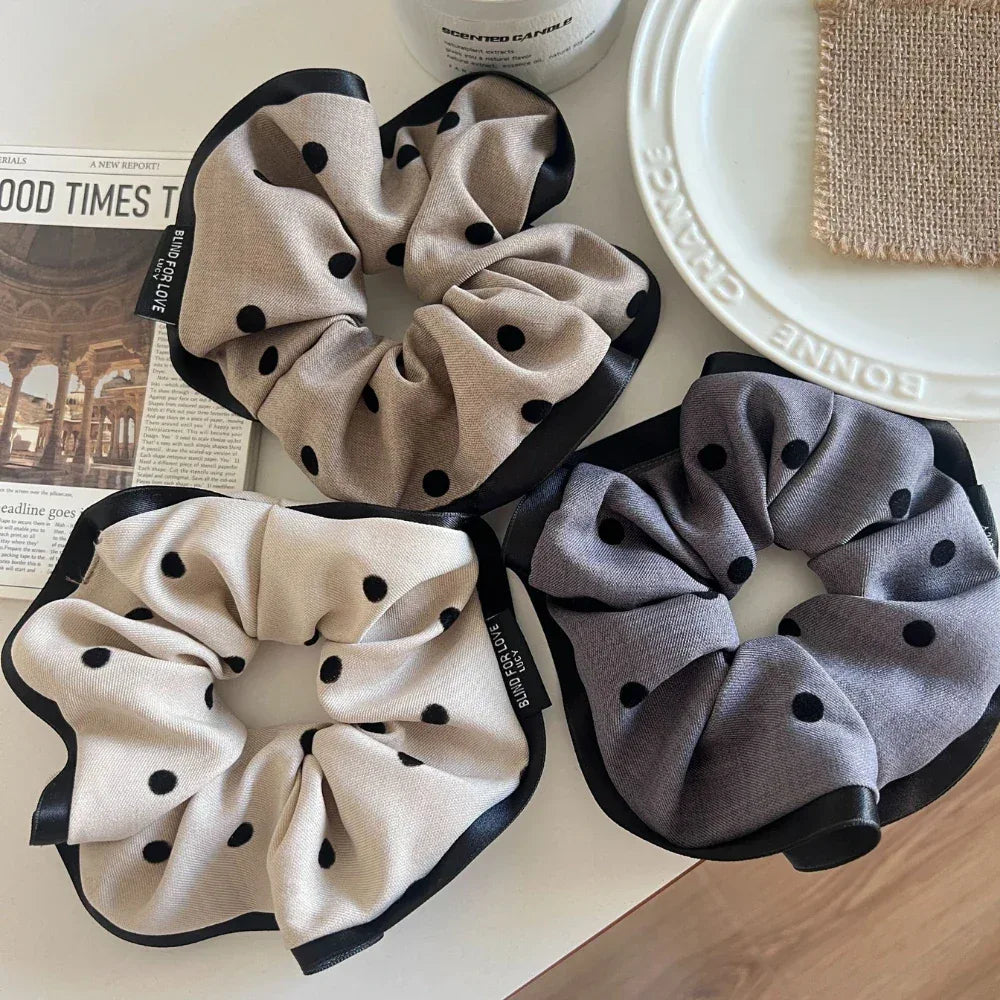 Three polka dot scrunchies, two beige and one gray, on a white surface with a newspaper