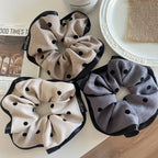 Three polka dot scrunchies, two beige and one gray, on a white surface with a newspaper
