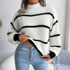 Woman wearing a white and black striped knit sweater with a high neckline and long sleeves, paired with light blue jeans.