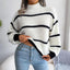 Woman wearing a white and black striped knit sweater with a high neckline and long sleeves, paired with light blue jeans.