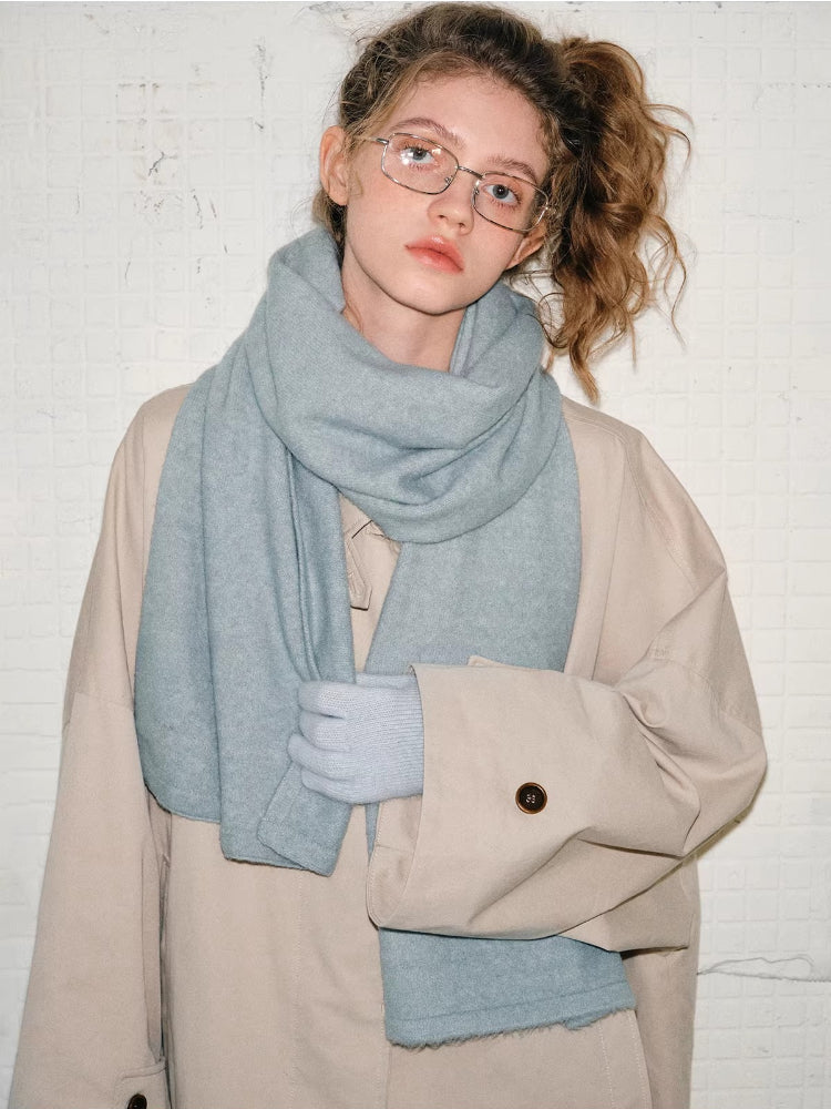 Model wearing a beige oversized coat with a light blue scarf and matching gloves. She is also wearing glasses.