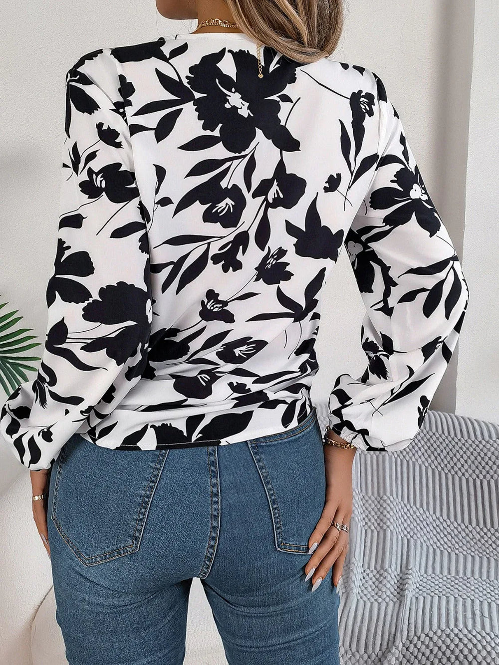 Woman wearing a black and white floral print long sleeve blouse with a front tie detail and blue jeans, back view