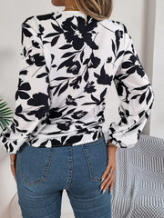 Woman wearing a black and white floral print long sleeve blouse with a front tie detail and blue jeans, back view