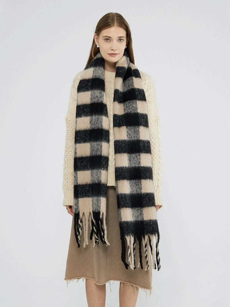 Woman wearing a cream cable knit sweater and a large black and beige plaid scarf with fringe.