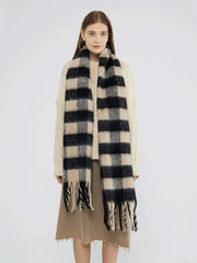 Woman wearing a cream cable knit sweater and a large black and beige plaid scarf with fringe.