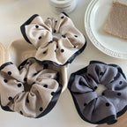 Three polka dot scrunchies, two beige and one gray, in a white container and on a white surface