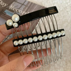 A hand holding a black hair comb adorned with white pearls, showing the comb teeth and the top decorative element.