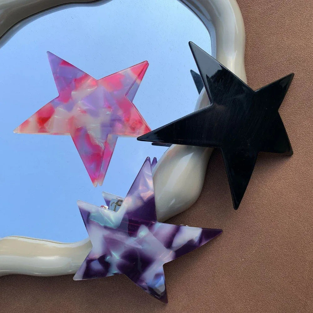 three star-shaped hair clips with marbled patterns and a black clip reflected in a mirror