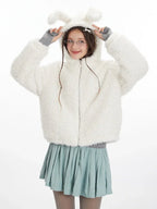 Front view of a model wearing a white fuzzy hooded jacket with bunny ears, a grey turtleneck, and a light blue pleated skirt. She is posing with her hands near the hood.