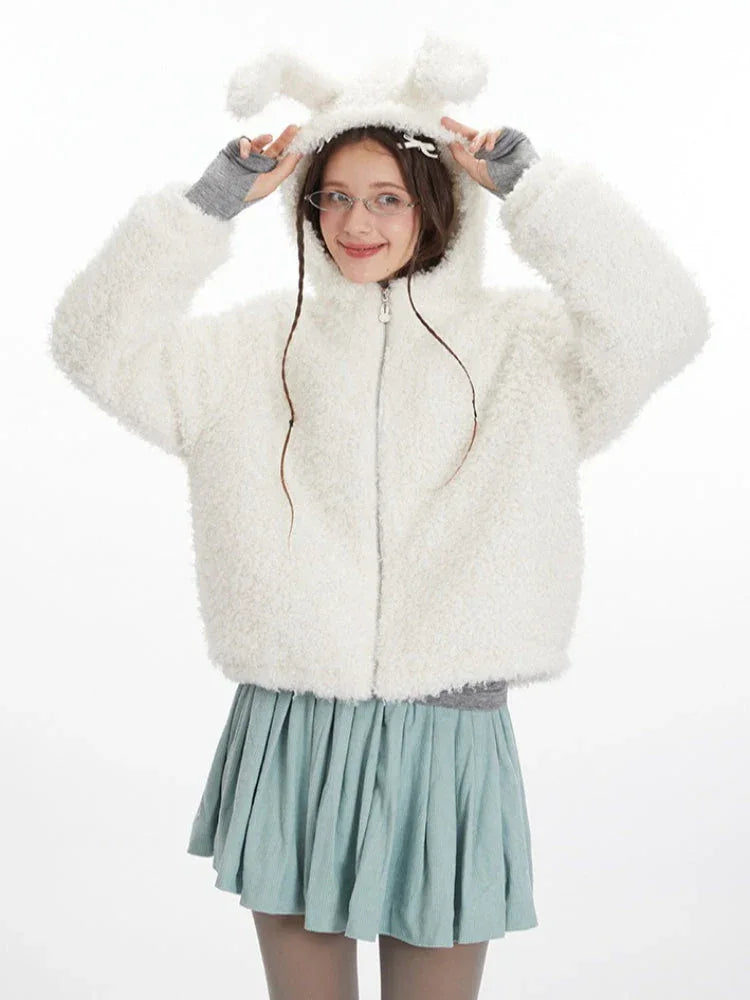 Front view of a model wearing a white fuzzy hooded jacket with bunny ears, a grey turtleneck, and a light blue pleated skirt. She is posing with her hands near the hood.