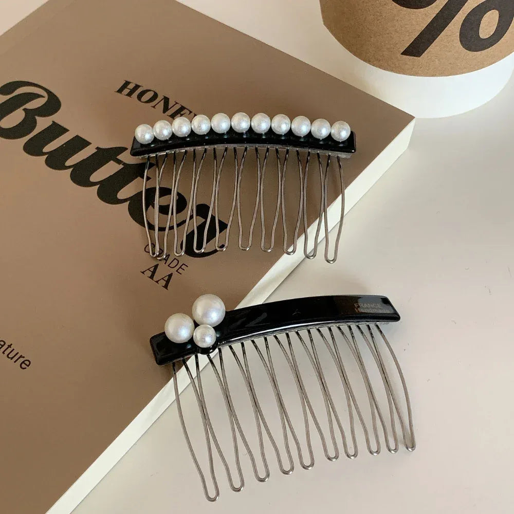 Two black hair combs with pearl embellishments are displayed on top of open books, one with a cluster of three pearls and the other with a row of pearls.