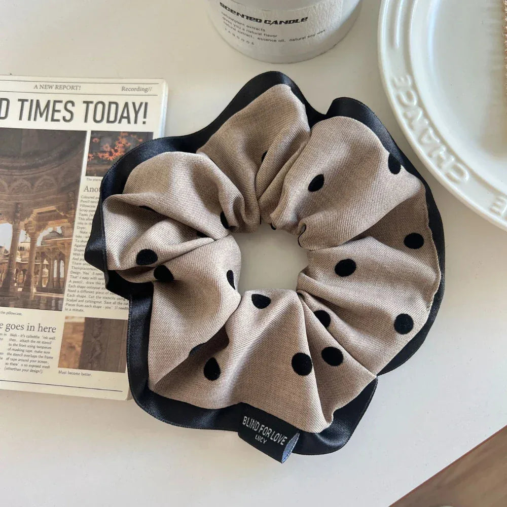 Beige polka dot scrunchie with black trim next to a newspaper
