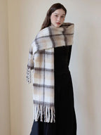Woman posing with a plaid scarf wrapped around her shoulders, showcasing the fringed ends and soft texture.