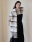 Woman posing with a plaid scarf wrapped around her shoulders, showcasing the fringed ends and soft texture.