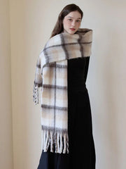 Woman posing with a plaid scarf wrapped around her shoulders, showcasing the fringed ends and soft texture.