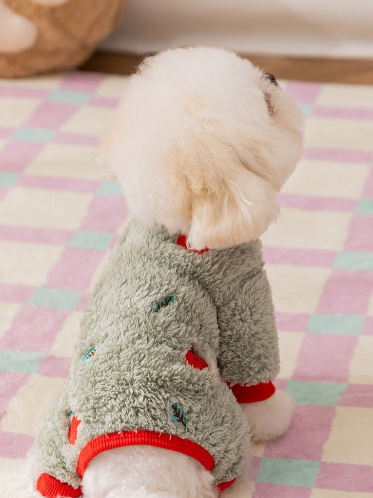 A rear view of a white Bichon Frise dog wearing a light green fleece dog jumpsuit with red cuffs and collar. The jumpsuit has a subtle all-over print of red and blue elements.