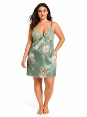 Full-body front view of a plus-size model in a green satin chemise featuring a floral print and lace neckline