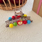 A transparent hair claw clip adorned with a red apple charm and a variety of colorful beads, displayed on a textured surface.