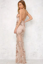 Woman in a long nude sequined and appliqued sheer dress with a high slit and deep V-neck, showing open back