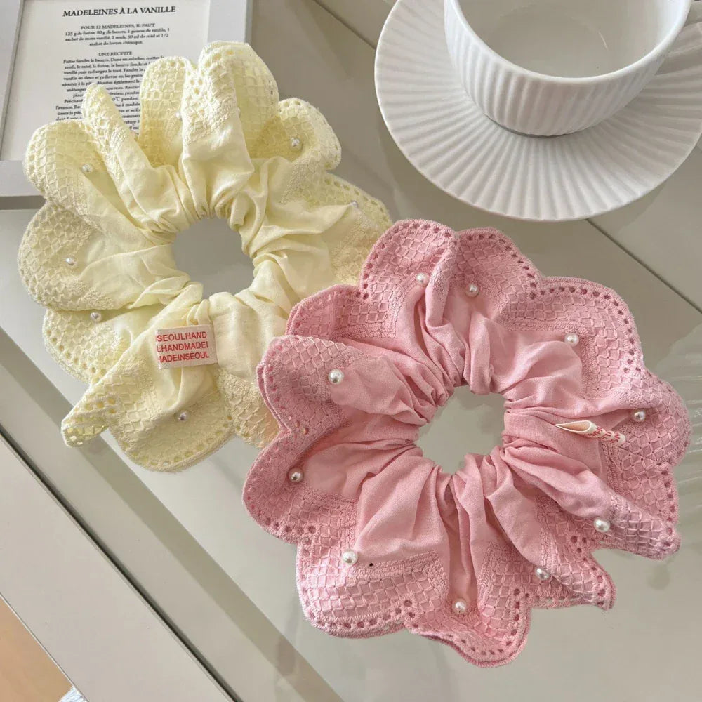 Yellow and pink scrunchies with lace and pearl details on a glass surface