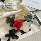 Several flower-shaped claw clips are artfully arranged on a textured fabric, with a mug, a tube of hand cream, and a folded card in the background.