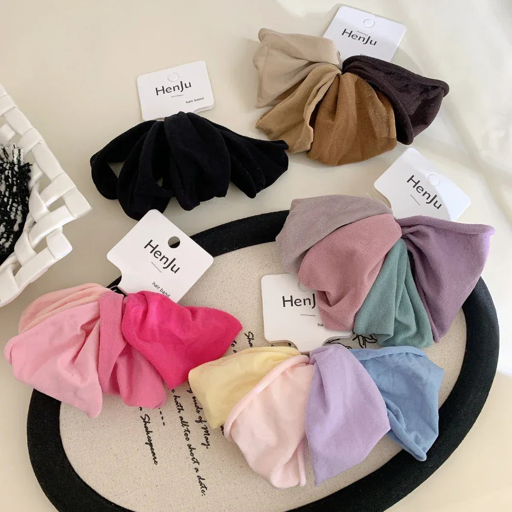 A variety of scrunchie sets in different colors, including pink, purple, blue, yellow, and brown, laid out on a surface.
